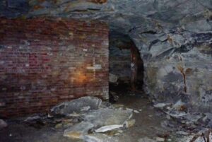 Dim underground scene with a red brick wall on the left and a dark rocky tunnel ahead, scattered rubble on the floor.