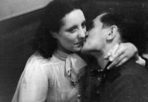 Black-and-white photo of a couple kissing closely, the woman wearing a light blouse with a bow at the neck.