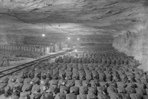 Underground mine storage area with rows of bundled sacks along a rail line and hanging work lights.