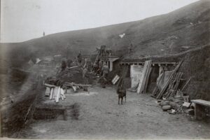 Soldiers work on a trench dugout along a hillside, with scattered planks and tools and a horse in the foreground.