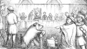 A bear chained to a wooden crate in a town square as a crowd of villagers and nobles watch from behind a railing.