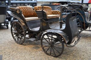 Vintage horse-drawn carriage with tufted tan leather seats on a gravel surface.