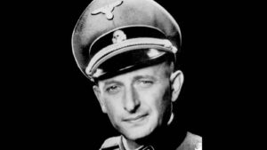 Black-and-white portrait of a man in a peaked military cap and uniform against a black background, facing slightly left.