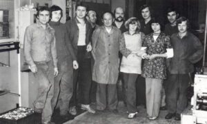 Group of coworkers standing together in a factory workshop, smiling at the camera and posing as a team.