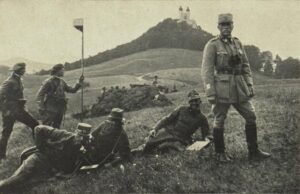 WWI-era soldiers in uniform on a grassy hill; one officer stands while others rest near a trench and a flag, with a hill and distant fort in the background