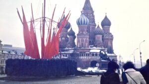 Red sculptural installation with tall red fins in a circular base, set in front of Saint Basil's Cathedral on Red Square, Moscow, with people walking nearby in winter.