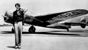Woman standing in front of a polished vintage jet on an airfield.