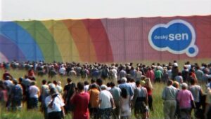 Large crowd of people facing a rainbow-colored wall with a blue cloud logo reading 'český sen' in the distance.