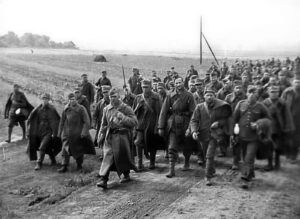 Group of soldiers in long coats marching along a dirt road in an open field.