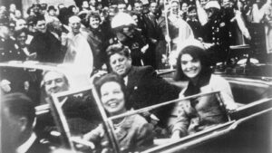 People in a vintage convertible waving to a cheering crowd during a parade, black-and-white photo.