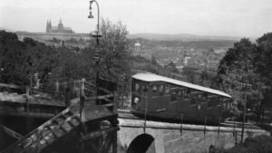 Vintage funicular car on a brick arched bridge overlooking a hillside town, with a cathedral visible in the distance and a wooden platform in the foreground.